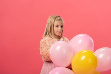 Sevimli ve şık çocuk pembe üzerinde izole edilmiş balonlar tutuyor. 