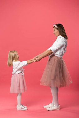 Gülümseyen kız ve annenin pembe arka planda el ele tutuşmalarının yan görüntüsü 