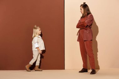 side view of daughter walking to mother with crossed arms on beige and brown background  clipart