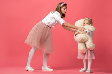 Anne, oyuncak ayıyı pembe arka planda gülümseyen kızına veriyor. 
