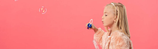 panoramic shot of cute kid blowing soap bubbles isolated on pink