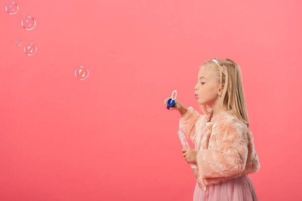 вид сбоку симпатичного ребенка, надувающего мыльные пузыри, изолированные на розовом
