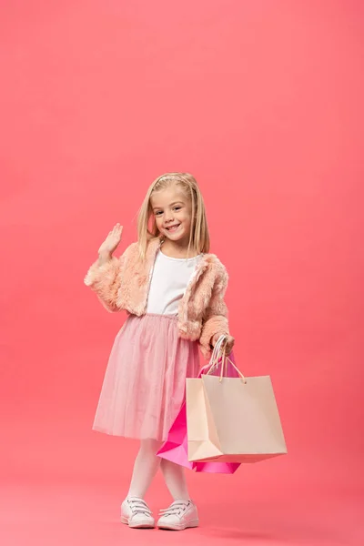 Bonito Sorridente Criança Acenando Segurando Sacos Compras Fundo Rosa — Fotografia de Stock