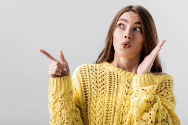 surprised girl pointing with finger while looking away isolated on grey clipart
