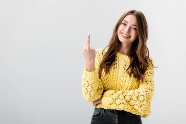 Gri üzerinde izole edilmiş orta parmağını gösteren neşeli kız kameraya bakıyor.