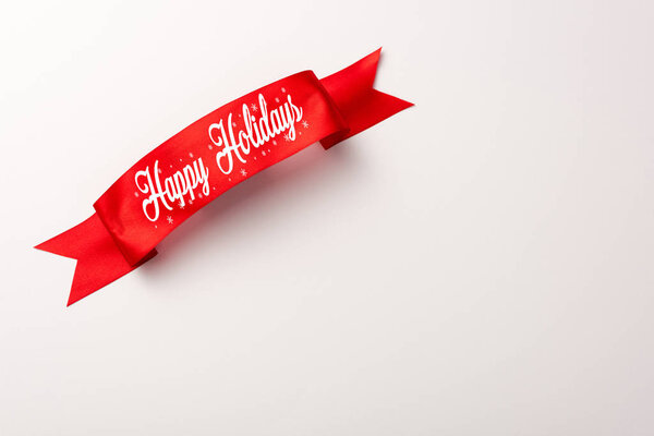 top view of red ribbon with happy holidays lettering on white 