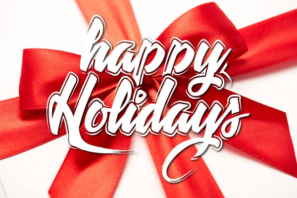 close up of satin ribbon with decorative red bow with happy holidays letters on white 
