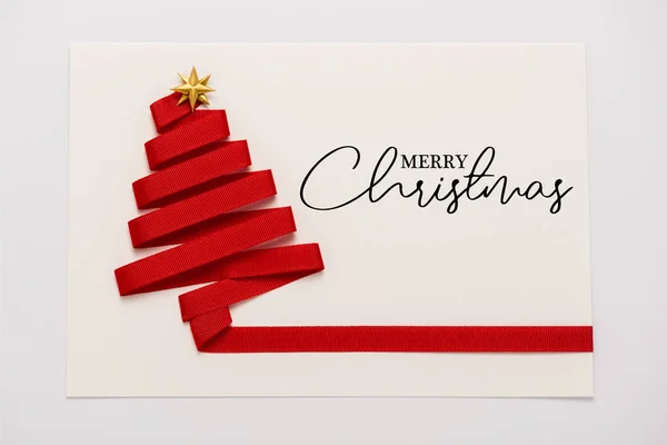 带金色星形蝴蝶结的红色缎带的顶视图 装在纸信封上 上面有用白色隔开的快乐圣诞信 — 图库照片