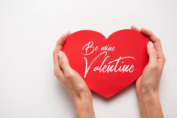 cropped view of woman holding red heart shape paper cut with be my valentine letters on white 