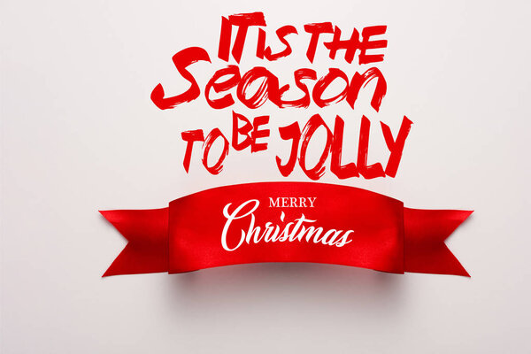 top view of red ribbon with its the season to be jolly, merry christmas lettering on white 