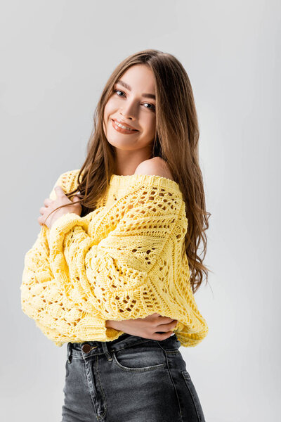 happy girl smiling at camera while hugging herself isolated on grey