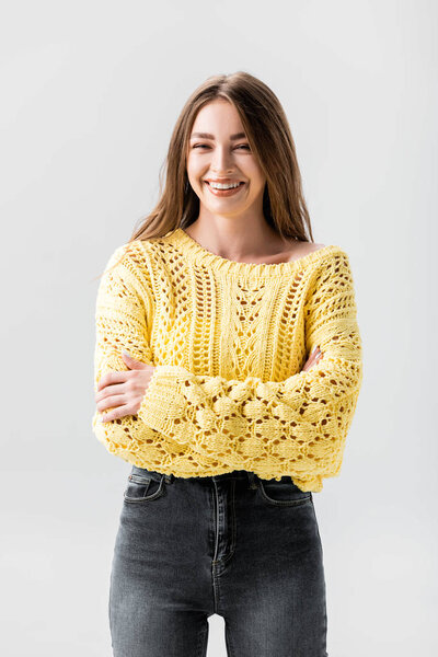 cheerful girl in yellow sweater standing with crossed arms isolated on grey