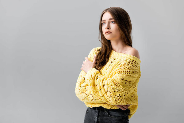 sad girl in yellow sweater standing with crossed arms and looking away isolated on grey