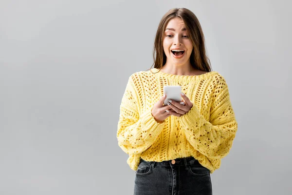 Zaskoczona Dziewczyna Żółtym Swetrze Patrząc Smartfon Odizolowany Szary — Zdjęcie stockowe