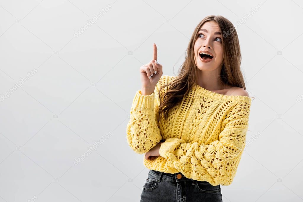 amazed girl pointing with finger while looking up isolated on grey