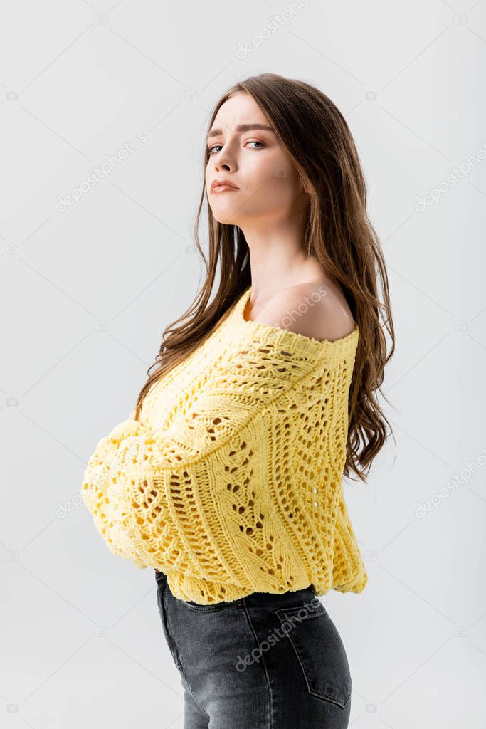 dissatisfied girl standing with crossed arms and looking at camera isolated on grey