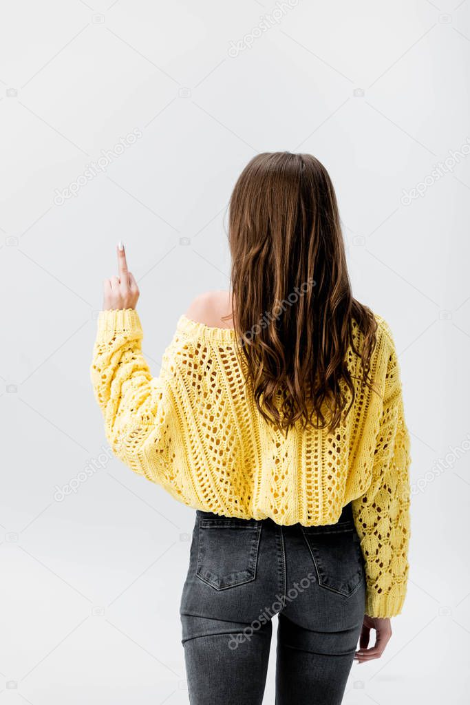 back view of girl in yellow sweater showing middle finger isolated on grey