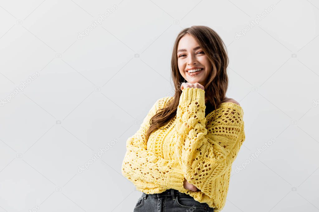 cheerful girl laughing and holding hand near face while looking at camera isolated on grey  