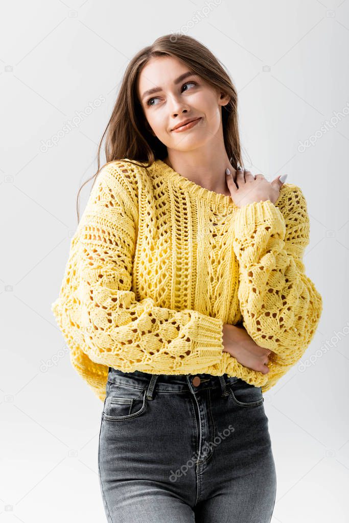 smiling, flirty woman looking away and touching shoulder isolated on grey