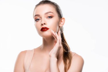 Güzel genç bir kadın beyaz kameraya bakarken yüzüne dokunuyor.