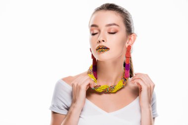 beautiful girl in beaded accessories, with beads on lips, touching necklace isolated on white