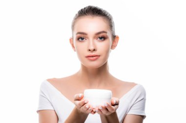 Çekici bir kız kameraya bakarken elinde yüz kremi kabı tutarken beyaz üzerine izole edilmiş.