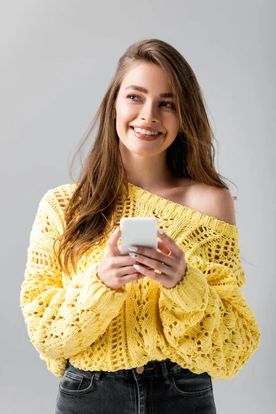 穿着黄色毛衣 面带微笑的女孩一边看一边用灰色智能手机把自己隔离起来 — 图库照片