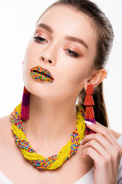 attractive girl in beaded accessories, with beads on lips, touching earring isolated on white