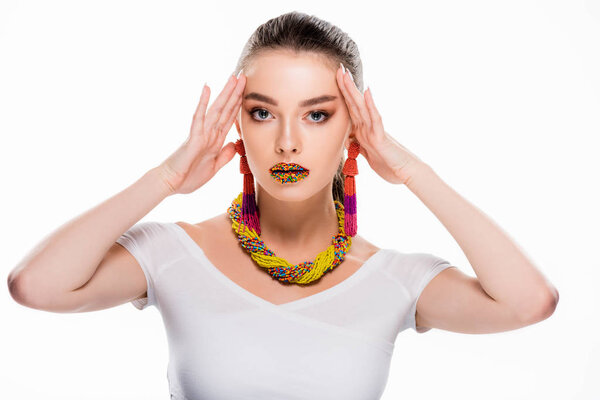 beautiful girl in beaded accessories, with beads on lips, touching head and looking at camera isolated on white