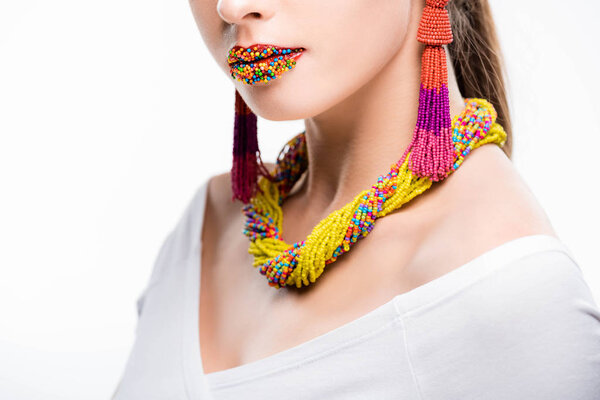 cropped view of girl in beaded necklace and earrings, with beads on lips isolated on white