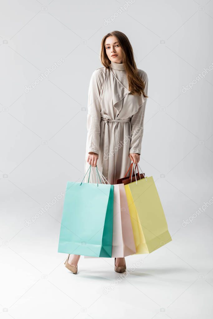 attractive, stylish girl looking at camera while holding shopping bags on grey background