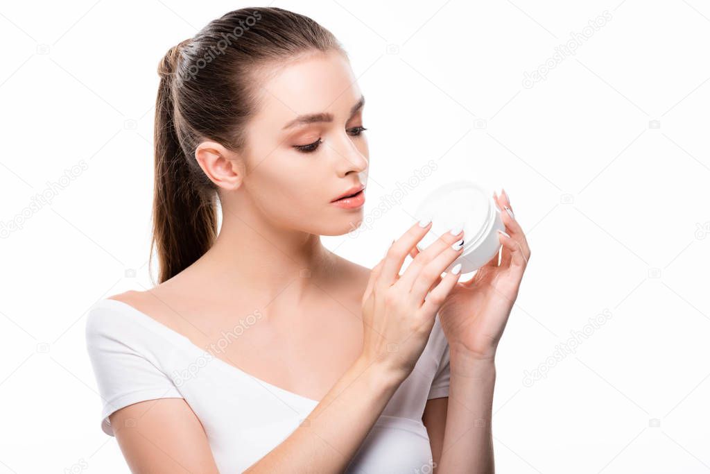 attractive young woman touching face cream in container isolated on white