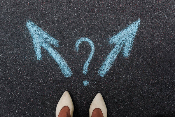 top view of woman standing near blue directional arrows and question mark on asphalt 