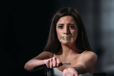 Ağzına yapıştırıcı bantla yapıştırılmış ve koyu arkaplandaki düz jiletle damarları keserek intihar eden kadın.