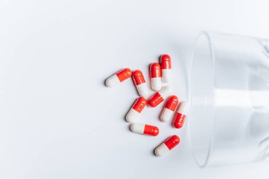 red and white capsules near overturned glass on white background, suicide prevention concept