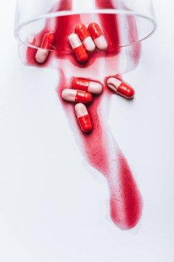 overturned glass and wet pills in red spills of water on white background, suicide prevention concept clipart