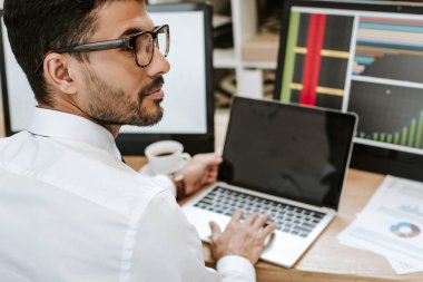 Laptop ve bilgisayarların yanında oturan çift ırklı tüccarın seçici odak noktası 