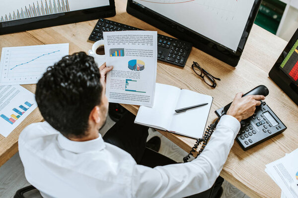 overhead view of bi-racial trader looking at paper and holding handset 