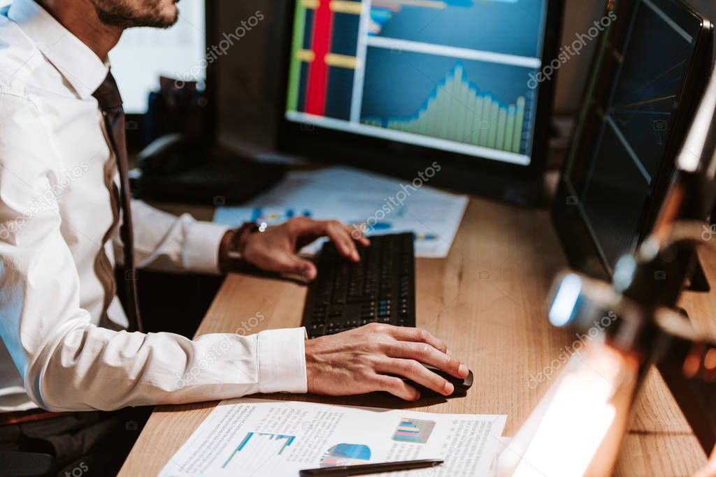 cropped view of bi-racial trader using computer and sitting at table 