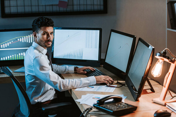 Двурасовый торговец, сидящий за столом и смотрящий в камеру
 