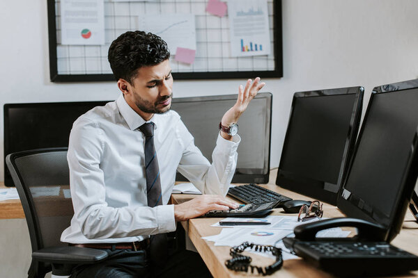 bi-racial trader using calculator and sitting at table in office  