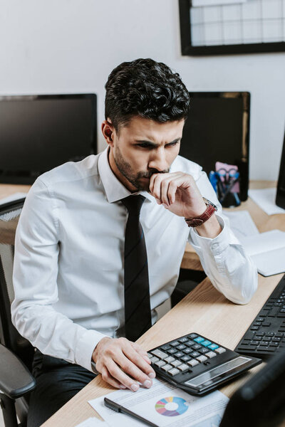 pensive bi-racial trader sitting at table and looking away 