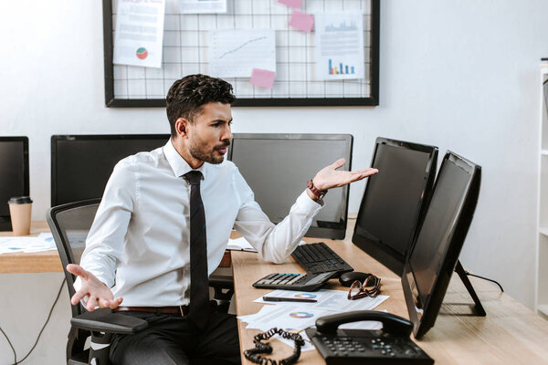 angry bi-racial trader pointing with hand at computer with blank screen 
