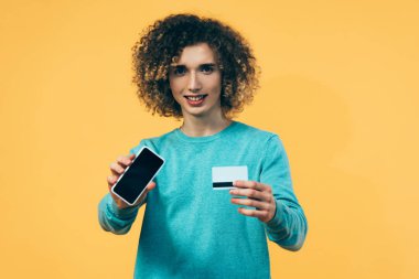 Akıllı telefon ve kredi kartı tutan kıvırcık ergen, sarıya izole edilmiş.