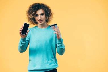 Akıllı telefon ve kredi kartı tutan kıvırcık ergen, sarıya izole edilmiş.