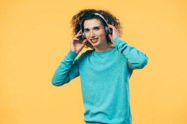 Gülümseyen kıvırcık ergen, sarı kulaklıkla müzik dinliyor.