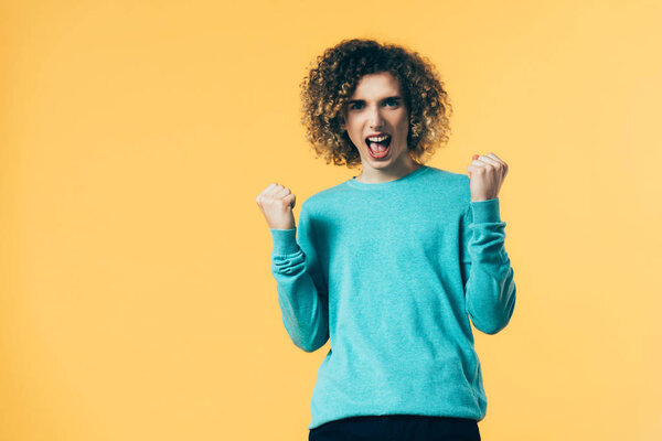 excited curly teenager screaming and showing yeah gesture isolated on yellow