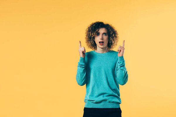 shocked curly teenager pointing with fingers isolated on yellow