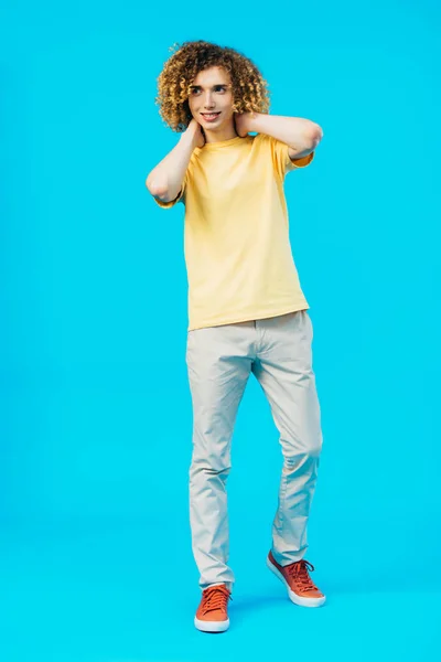 Sorrindo Encaracolado Adolescente Posando Com Mãos Atrás Pescoço Isolado Azul — Fotografia de Stock