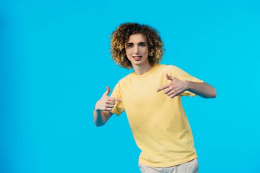 curly teenager pointing with fingers at himself isolated on blue clipart
